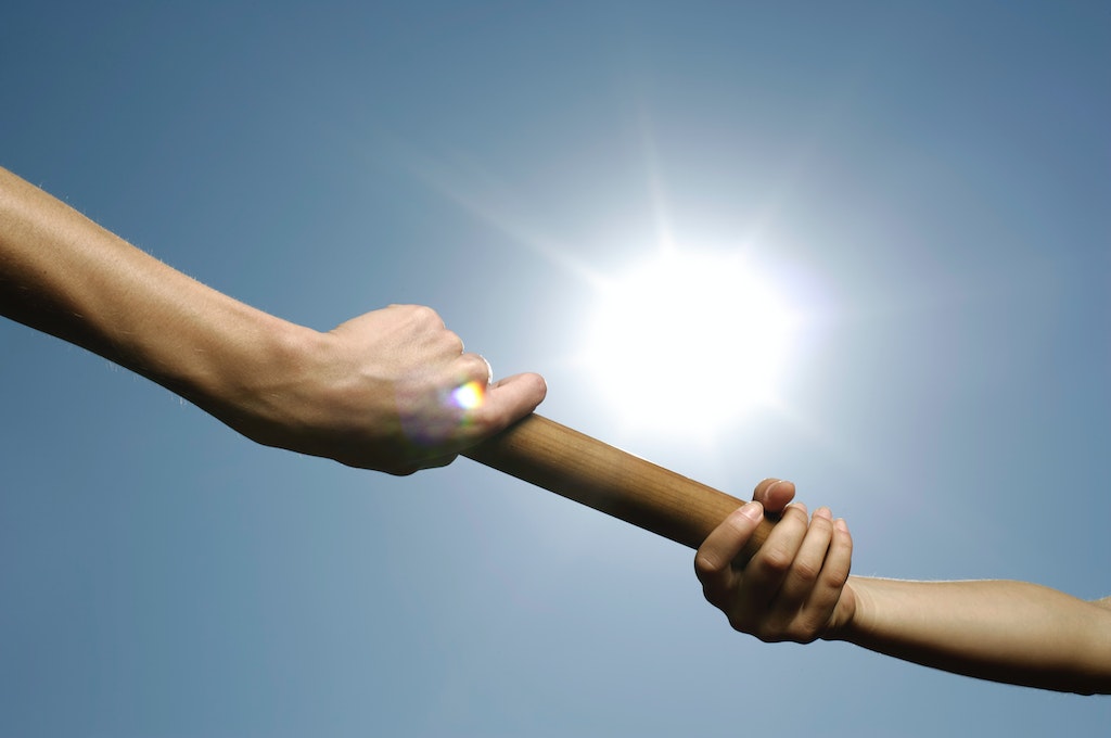 One hand passing the baton to another_leadership transition