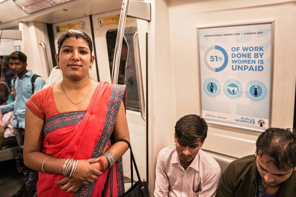 A woman standing in a metro beside a poster saying '51 percent of work done by women is unpaid'_female labour force participation