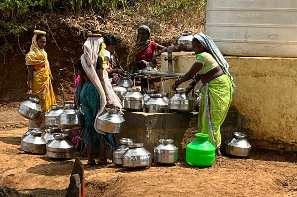 Four women gathered around a tap trying to fill their steel pots with water_water scarcity
