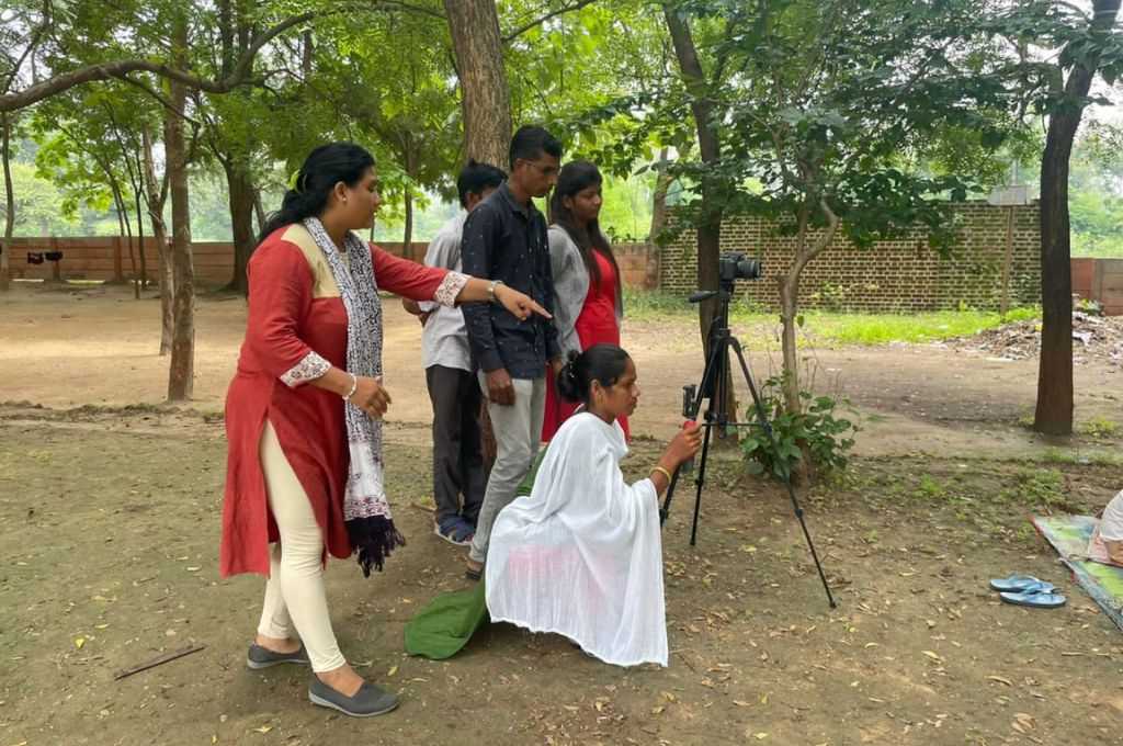 A woman shooting from a camera in a park with people surrounding her_Adivasi communities