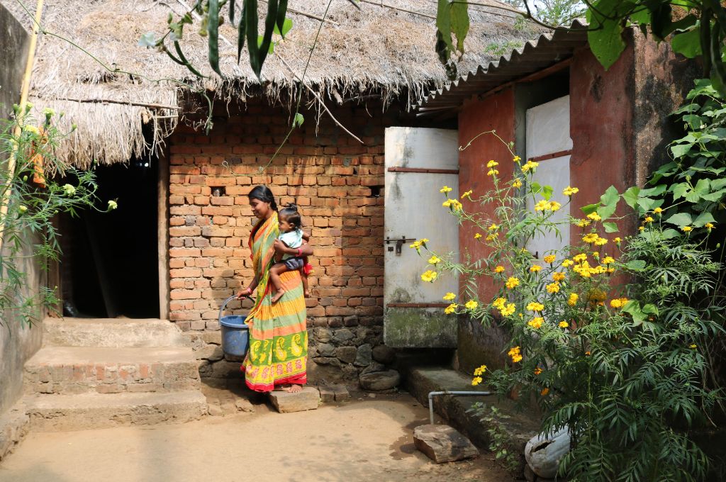 a woman in front of a house carrying a baby-rural women
