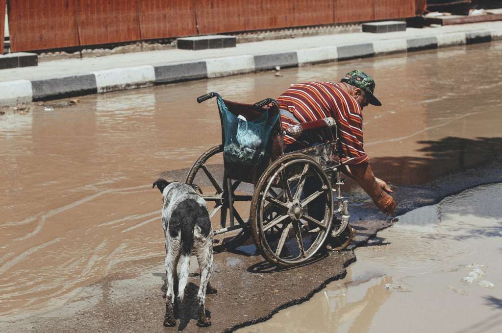 man in a wheelchair with a dog on a flooded road--persons with disability