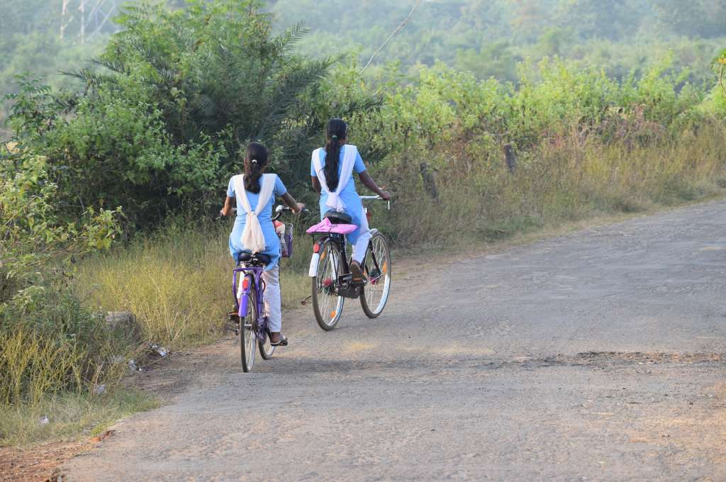 two girls in school uniforms riding their  bicycles on a road--outcome-based financing