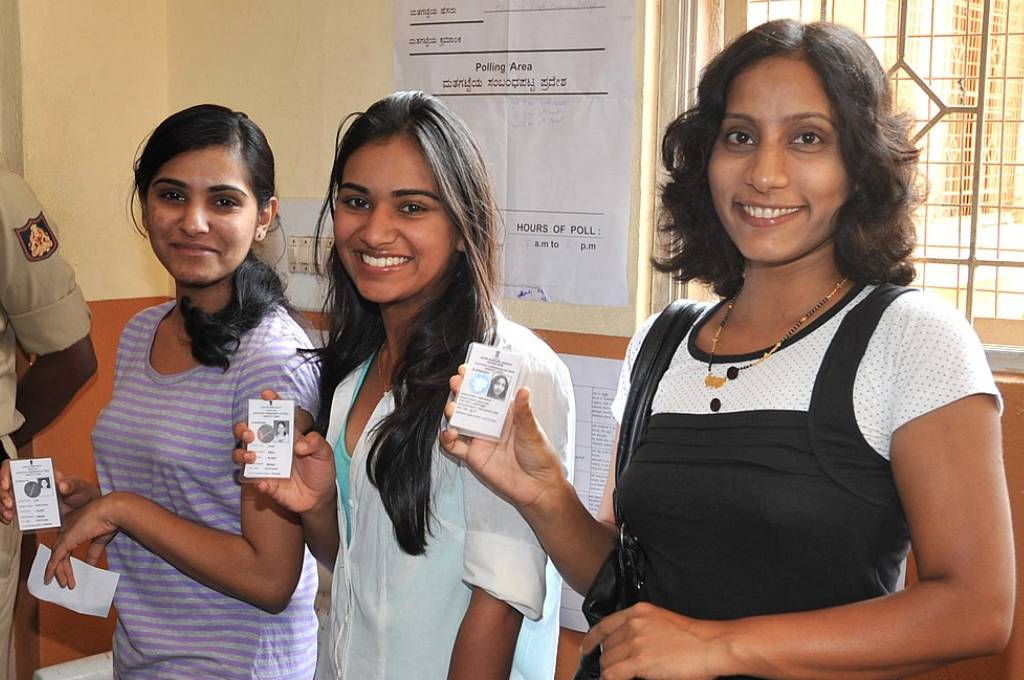 three young women holding up their identity cards at a polling booth--karnataka elections