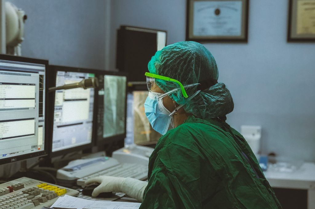 A doctor covered in green uniform and mask looking at computers_ayushman bharat