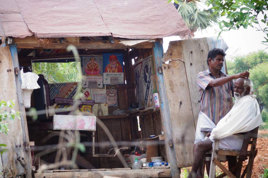 A barber and his client sit in front of the barber shop_poverty 