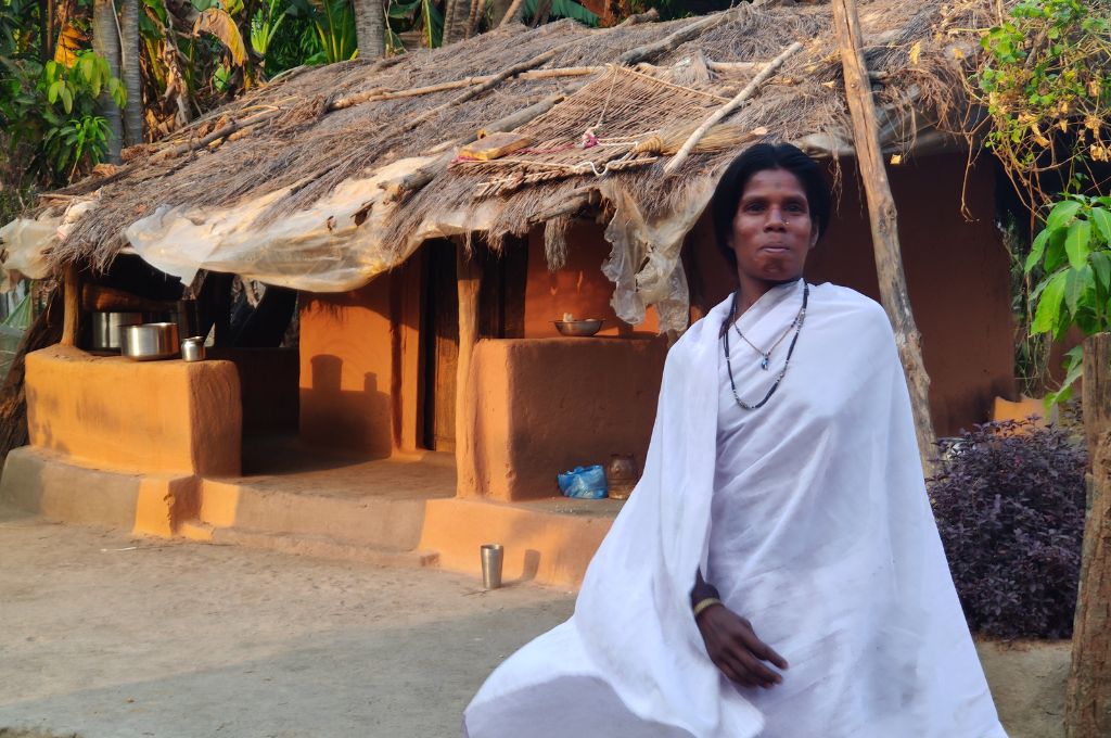 a woman from the Bhunjia community standing in front of a hut