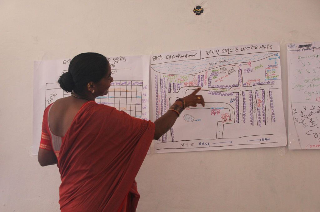 A woman explaining the layout of her village on a handrawn map on the wall--climate