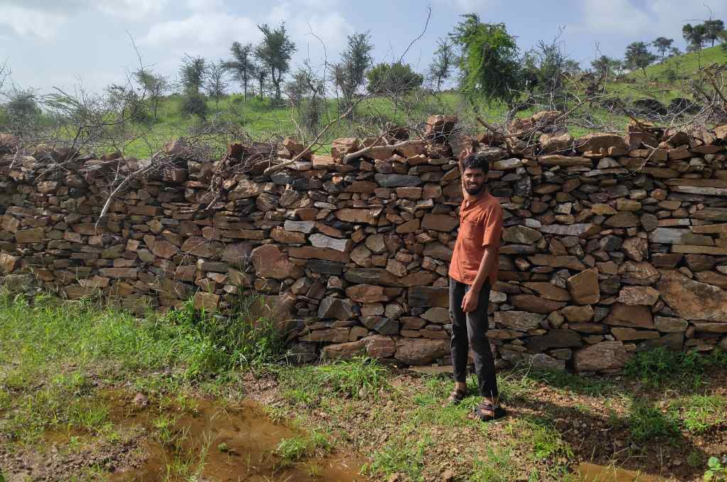 a young man standing in front of a stone wall--common land