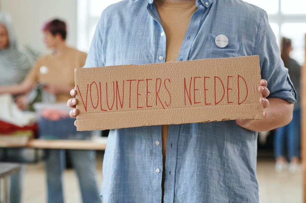 a woman holding a placard that says "volunteers needed"_fundraising