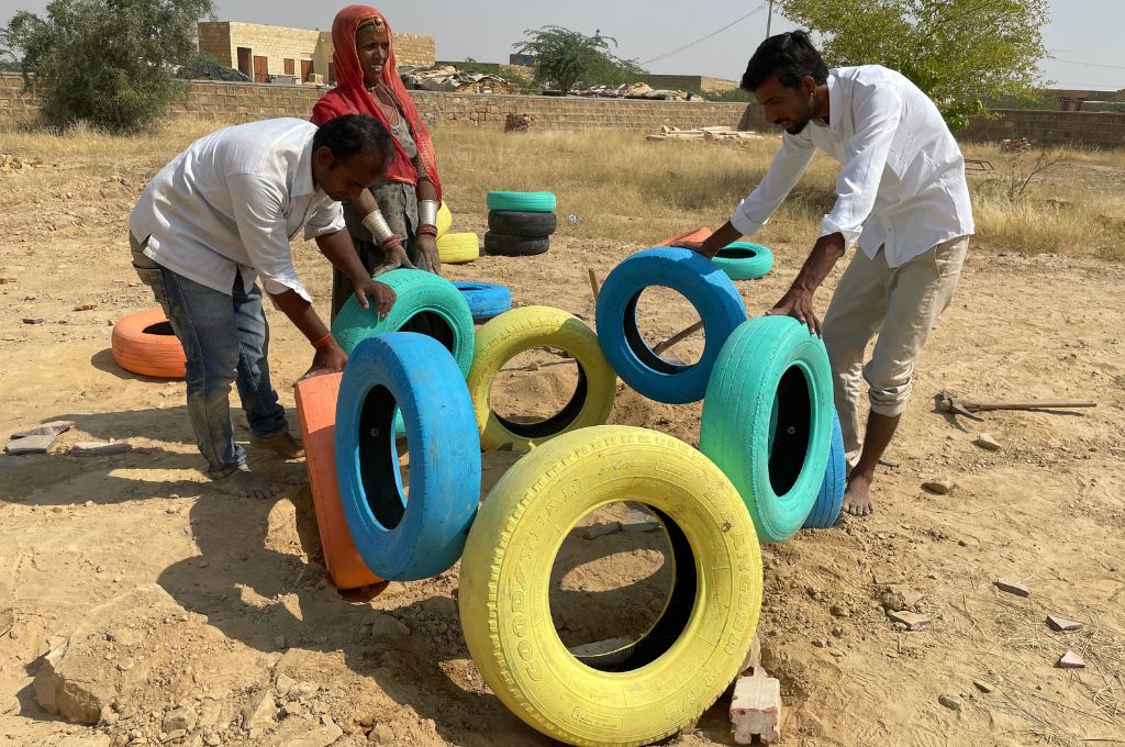two men hold painted-over tyres as a woman looks on--Rajasthan architecture