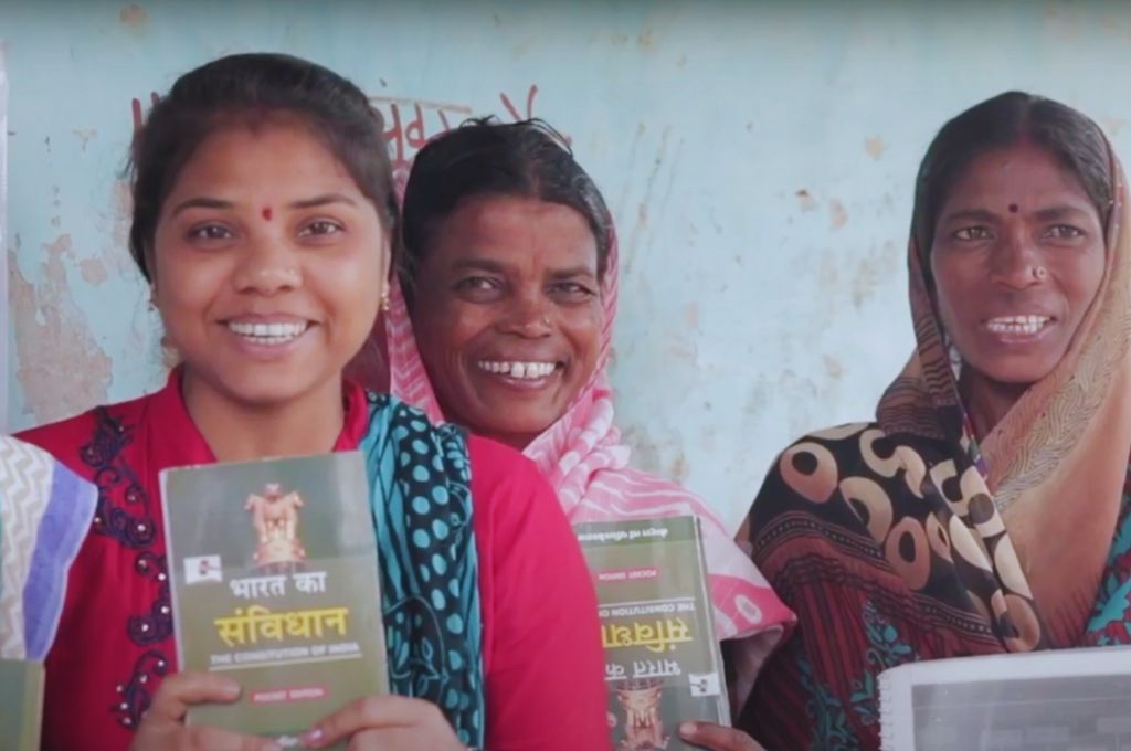 three women smiling and holding up copies of the Indian Constitution--active citizenship