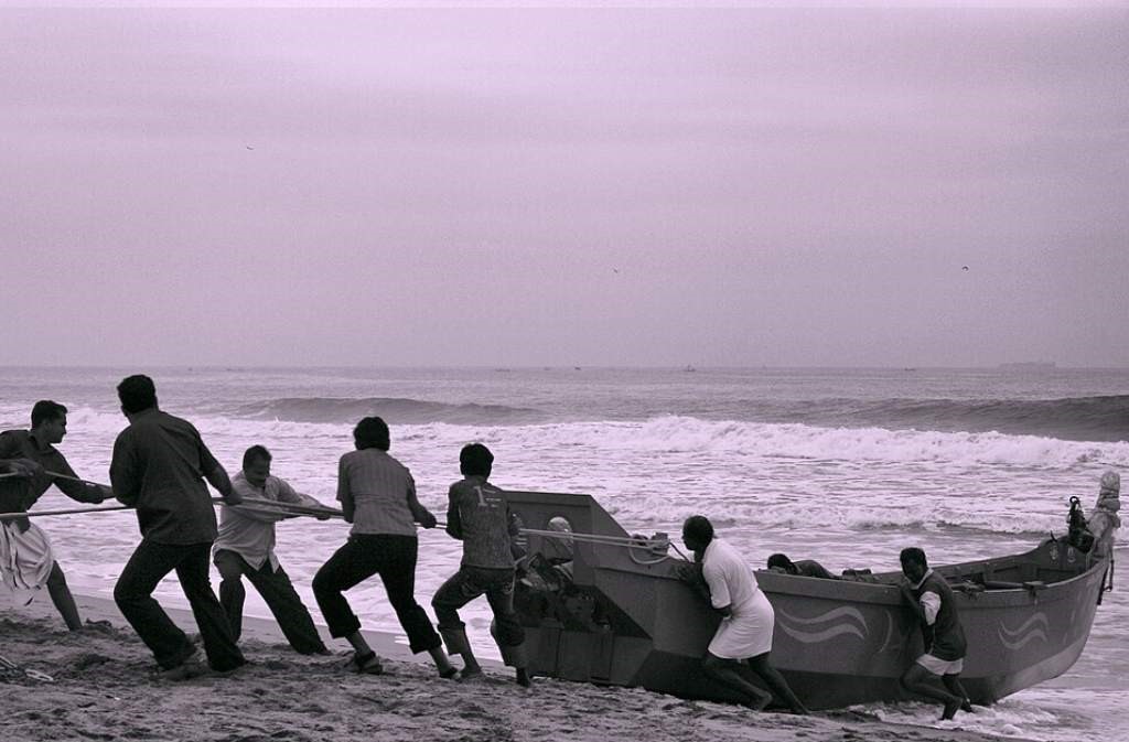 men pulling out a boat together from the ocean-community volunteering