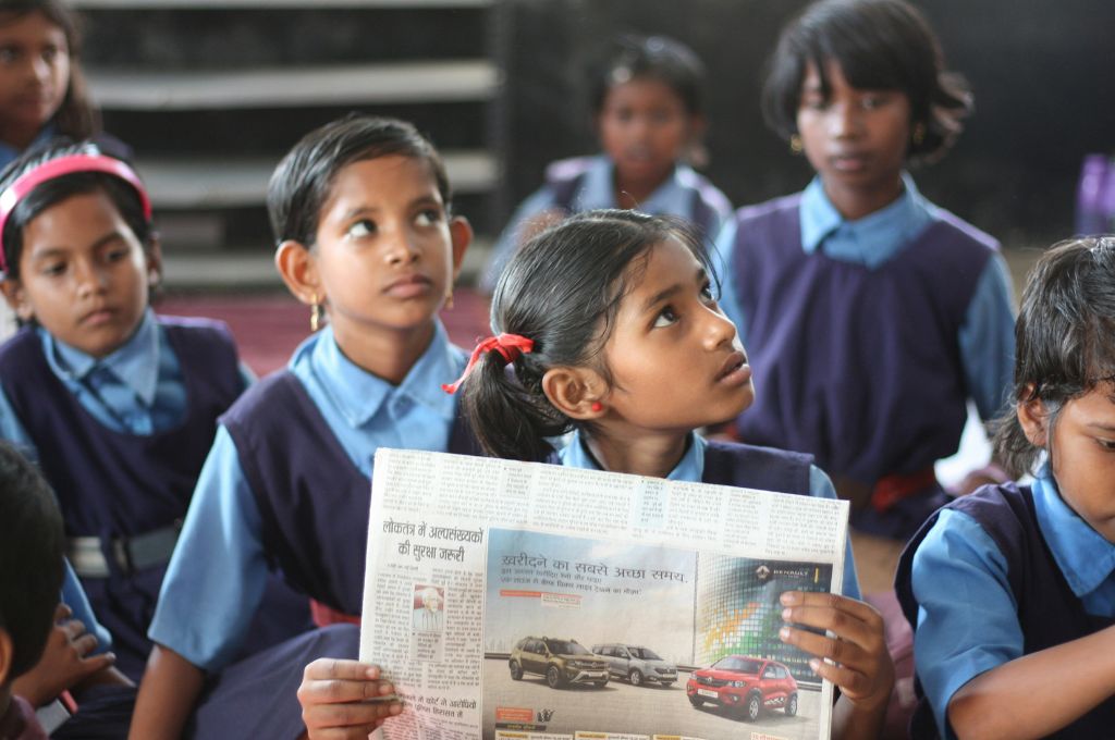 a girl in a classroom holds up a newspaper--ASER survey