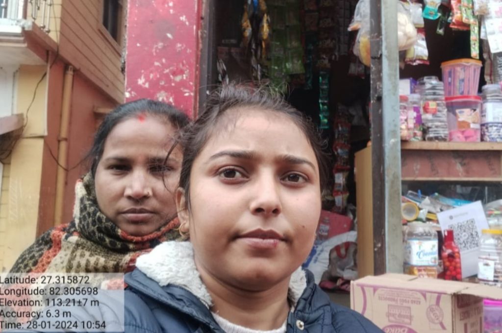 two women take a selfie in front of a kirana store--rural working women