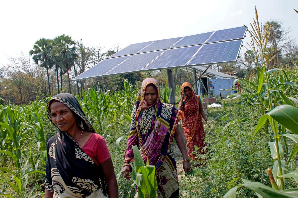 women in a field walking in front of a solar panel_renewable energy