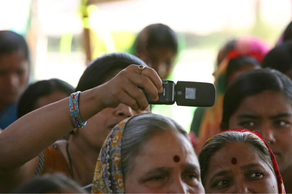 A woman in a crowd filming with a flip phone-technology