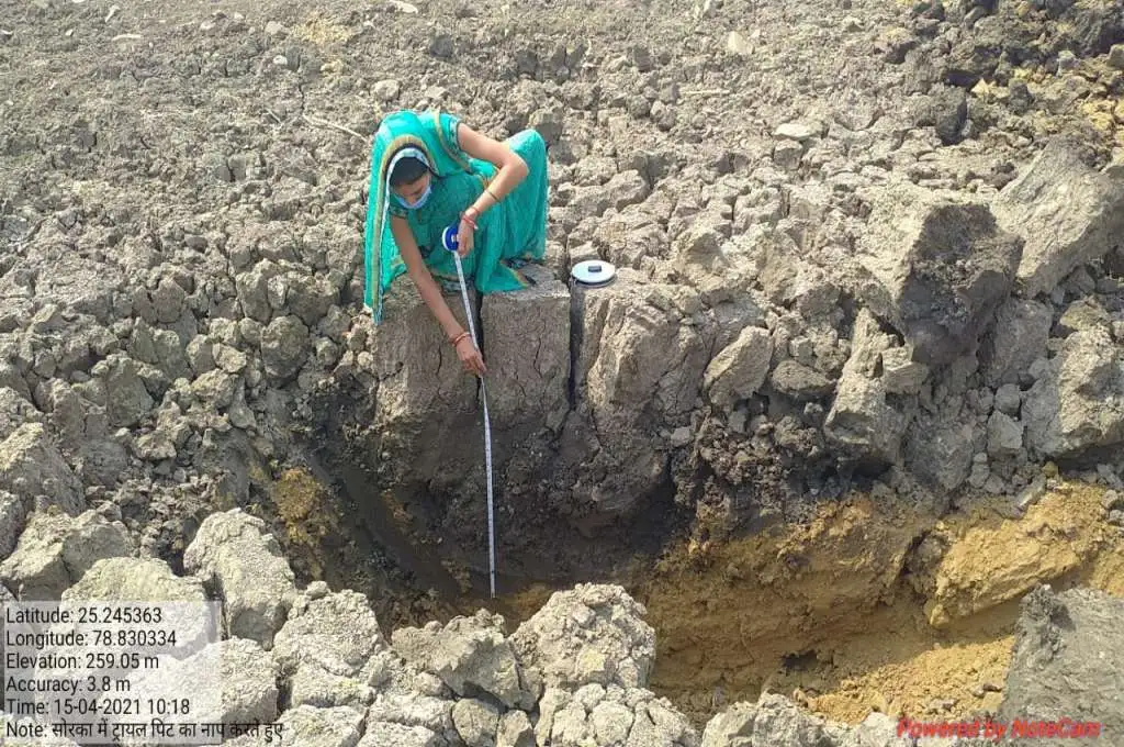 A woman extends a measuring tape into the trial put dug in the Sorka village to assess its composition - Water management