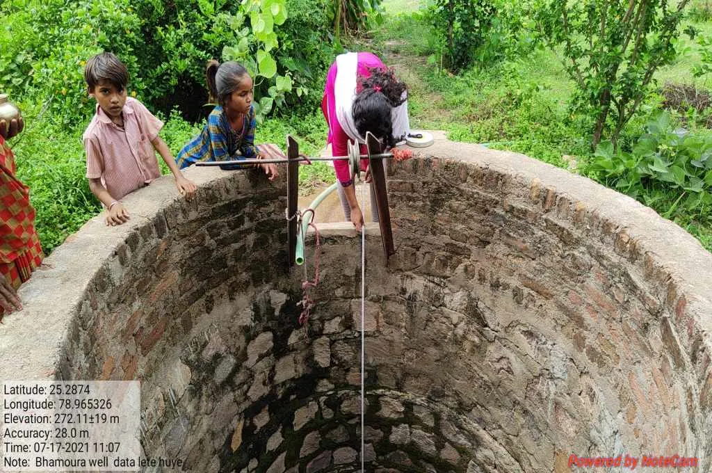 A woman extends a measuring tape into a well to monitor the groundwater level as two children stand beside her- Water management