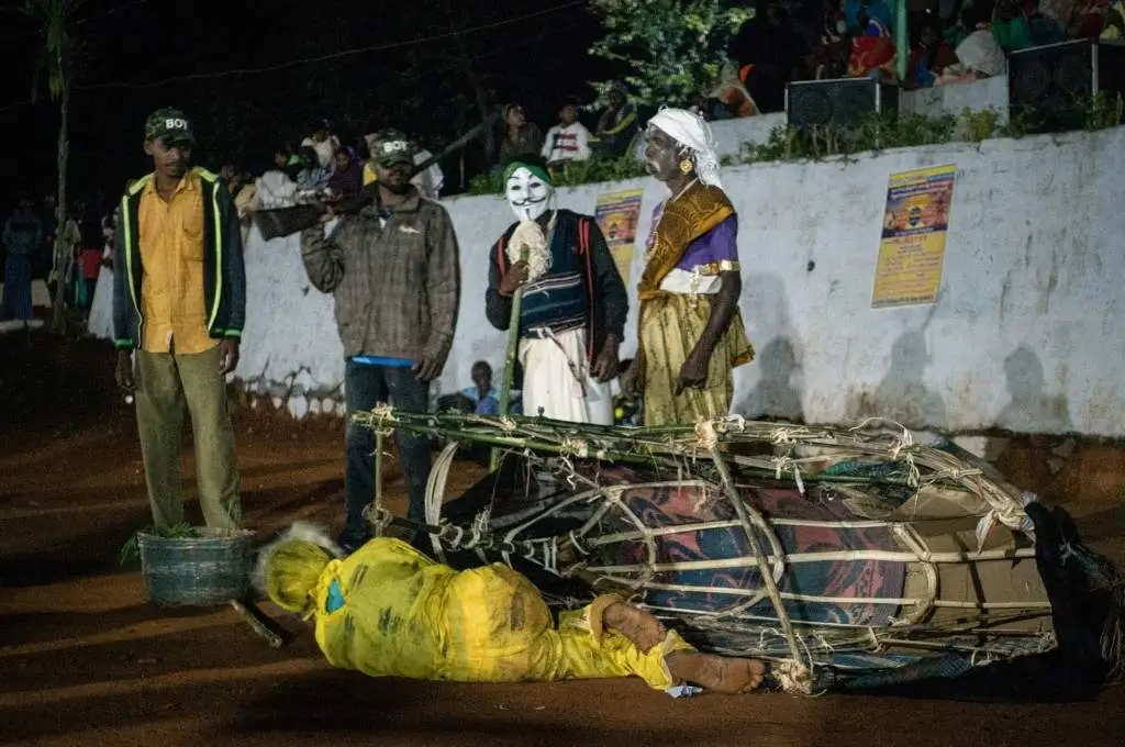 the performers portraying the forest officials in a doddu aatam play standing beside the performer playing a dead tiger--irula tribe