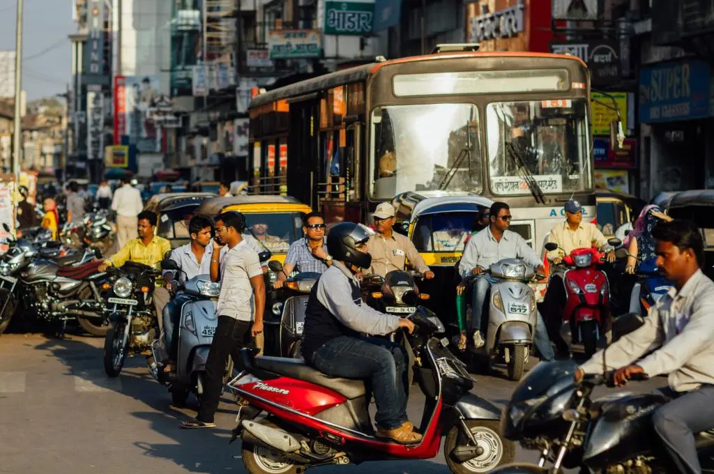 A bus, autorickshaws, and people riding two-wheelers wait in traffic. - Low emissions zones