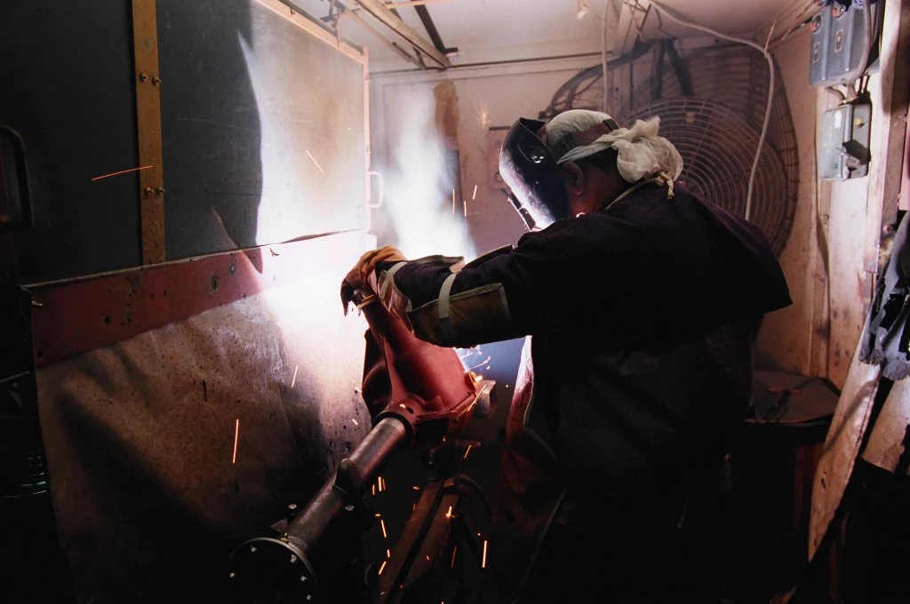 A man uses industrial machinery to work on a metal part for a vehicle. - Skill development