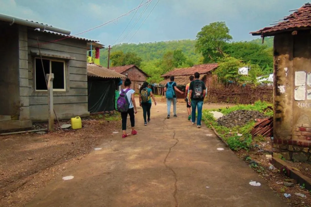 A group of people walk down an unpaved street in a rural area - Drug rehabilitation