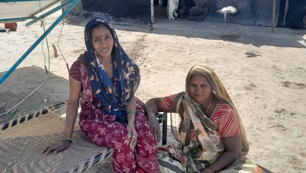 a photo of two women sitting next to each other, the younger one on a cot and the older one on the floor--salt farming