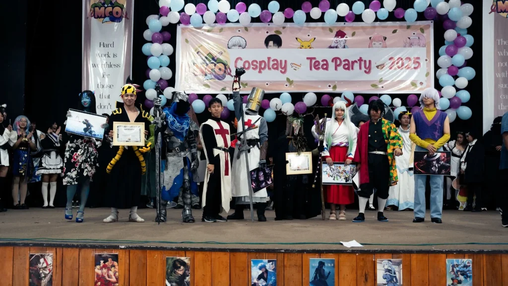 A group of cosplayers standing on a stage with a banner saying 'Cosplay Tea Party' in the background--cosplay in Mizoram
