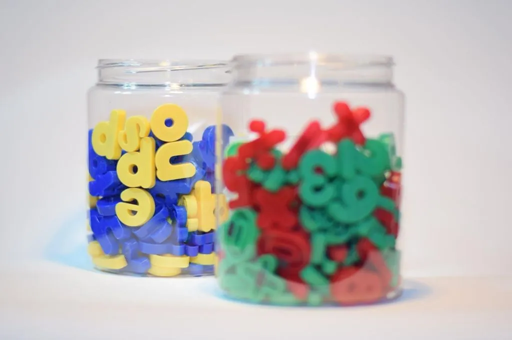 two glass jars, with one in the front containing numbers in red and green colours and the one in the back containing letters of the alphabet in yellow and blue--foundational literacy and numeracy