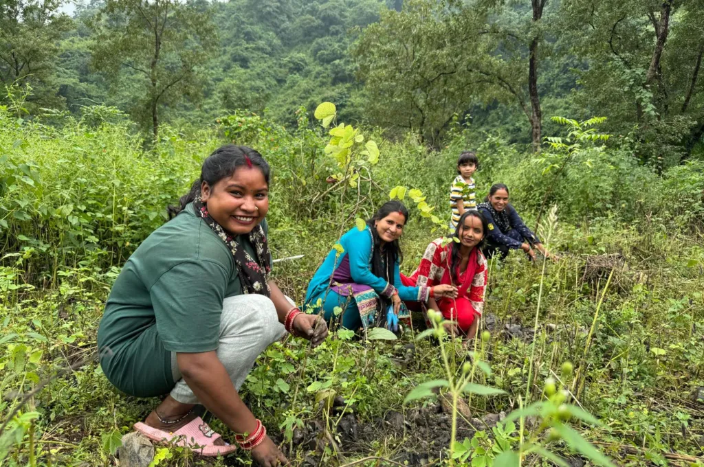four women and a child sitting in a field with dense tree cover in the background--paryavaran sakhis