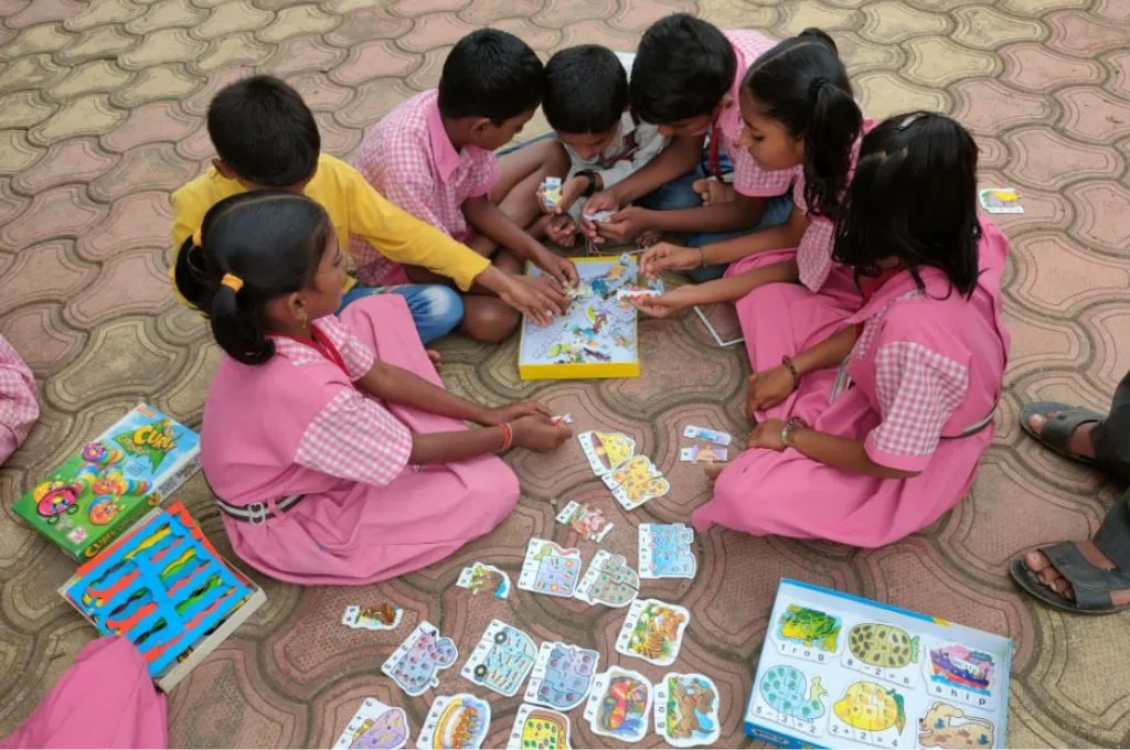 a group of school children sitting on the floor. They have images spread out around them and in front and they are playing with them