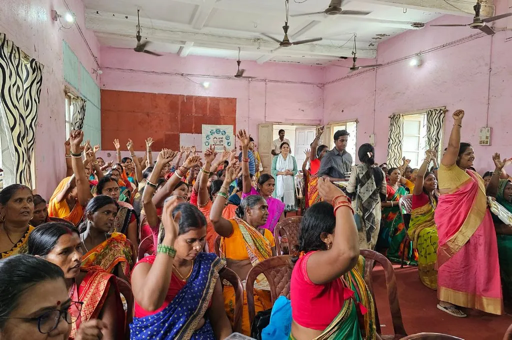 a group of women seated in a hall with their hands raised--Farmer Producer Organisations (FPOs)