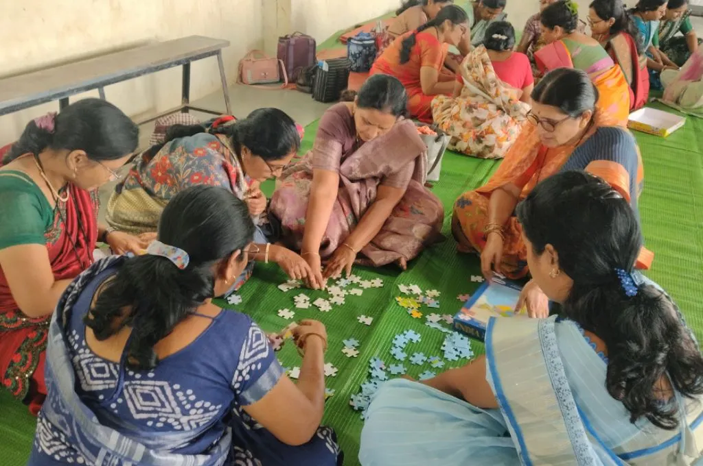 a group of women sitting on a green mat and collaboratively assembling a jigsaw puzzle during a workshop--early childhood education