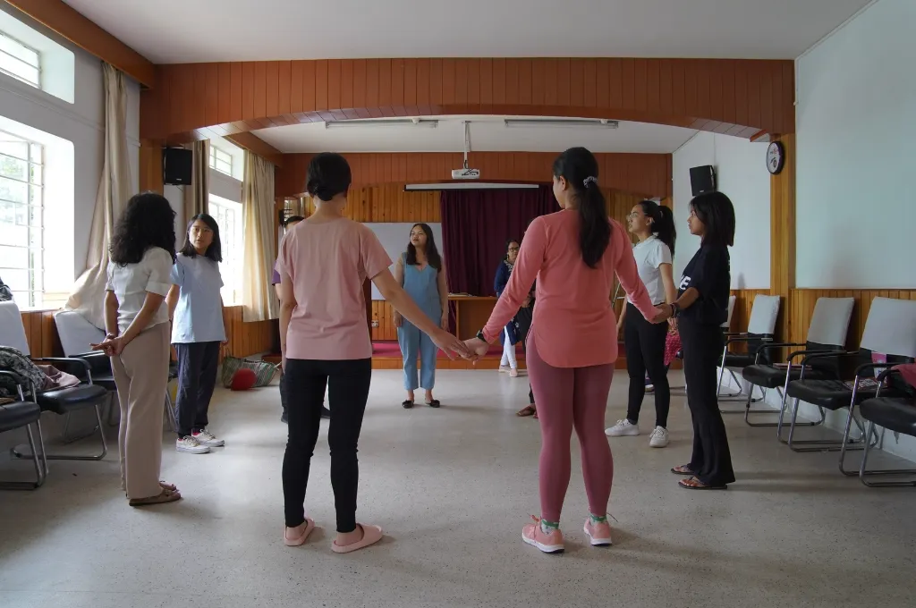 Women standing in a circle in a brightly lit room holding hands--counsellors