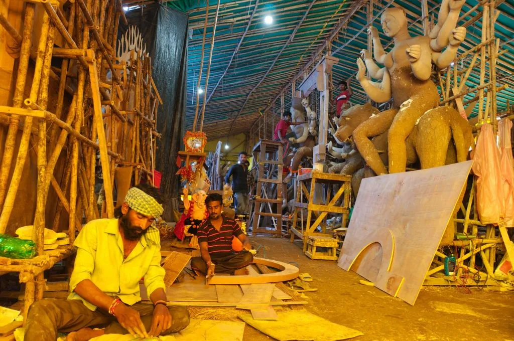 artisans making idols of hindu gods in a workshop, with idols in the background in various stages of completion--pollution