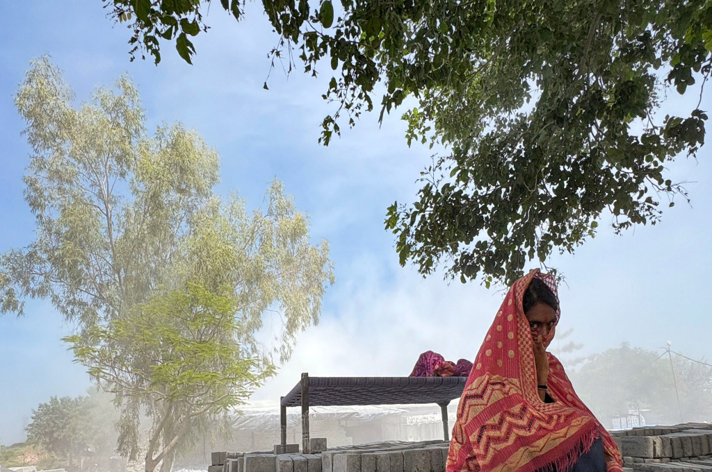 A worker covers her face with a shawl, with fly ash everywhere in the background--fly ash