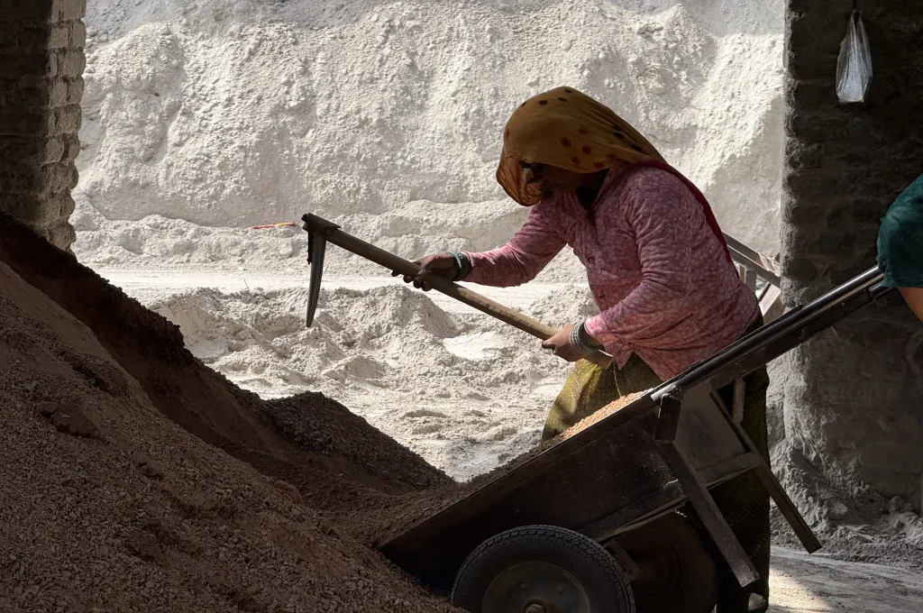 A female worker with her face covered mixing materials to make fly ash bricks​​--fly ash