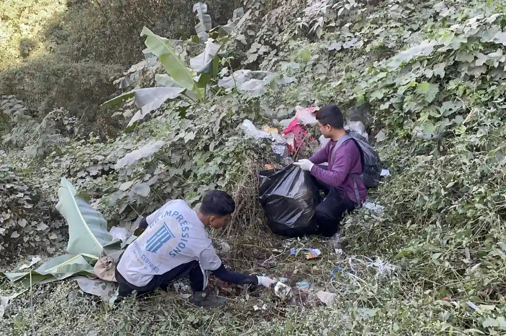 two male members of save the riparian, a river cleaning group in mizoram, picking solid waste on a hillside--river cleaning