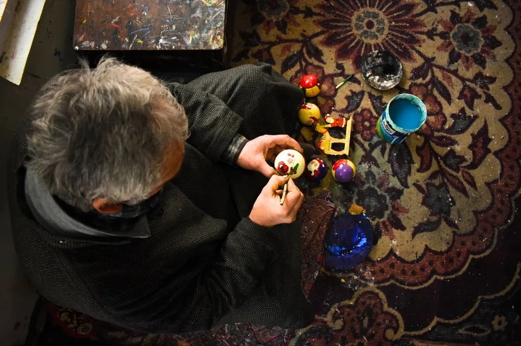 A paper-mache artist using a brush to paint different colours and figures on Christmas baubles.--paper-mache in Kashmir