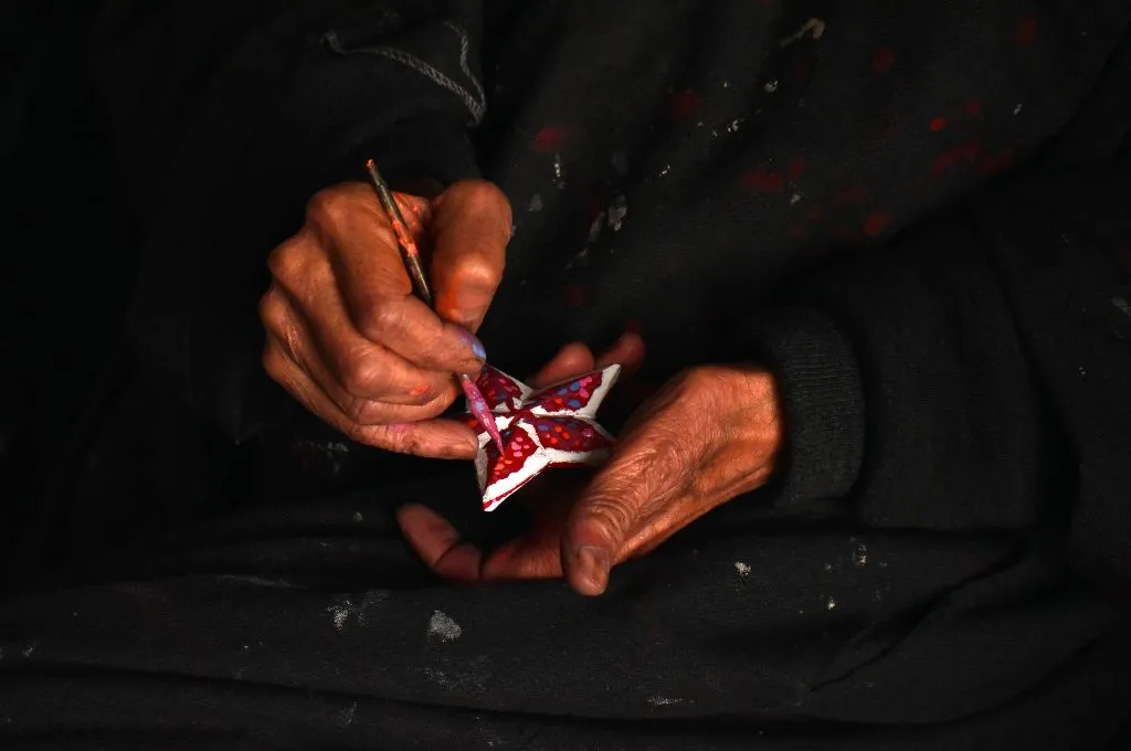 A close up of an artisan's hands painting a paper-mache ornament--paper-mache in Kashmir