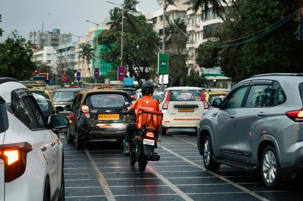 a motorcyclist in an orange Swiggy shirt driving through traffic--gig workers