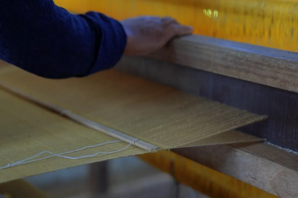 the hand of a person placed on a wooden beam on an eri silk loom--eri silk