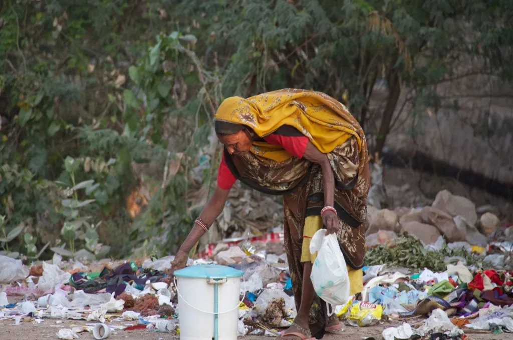 A woman in a yellow saree collecting solid waste from the ground_waste management
