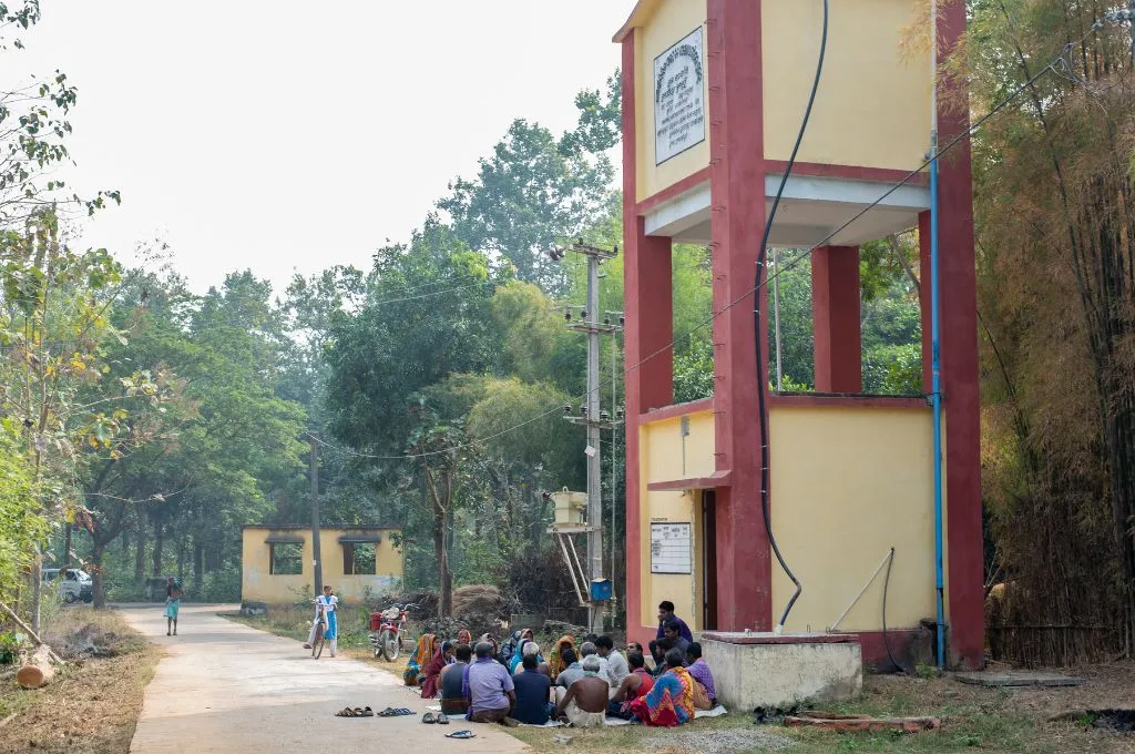 a group of people sitting outside a building with trees in the background--rights and development
