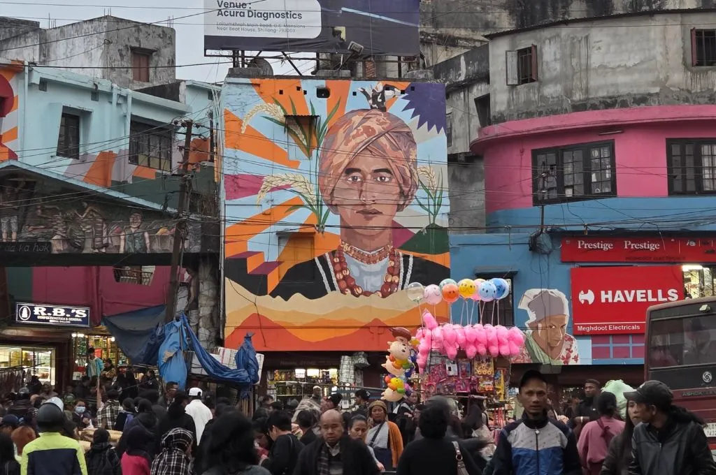a busy market in shillong with a large mural of a man in traditional clothing in the backdrop--street vendors