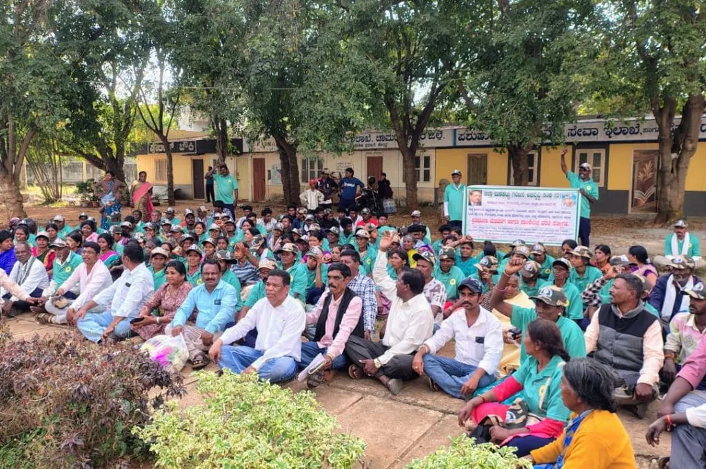 a group of people sitting outdoors under trees during a meeting, with a banner in the back--Tribal health