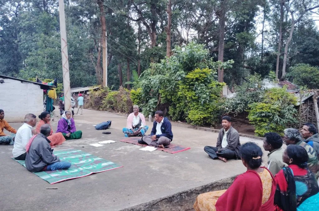 people sitting on the ground in a circle with trees in the background--community forest rights