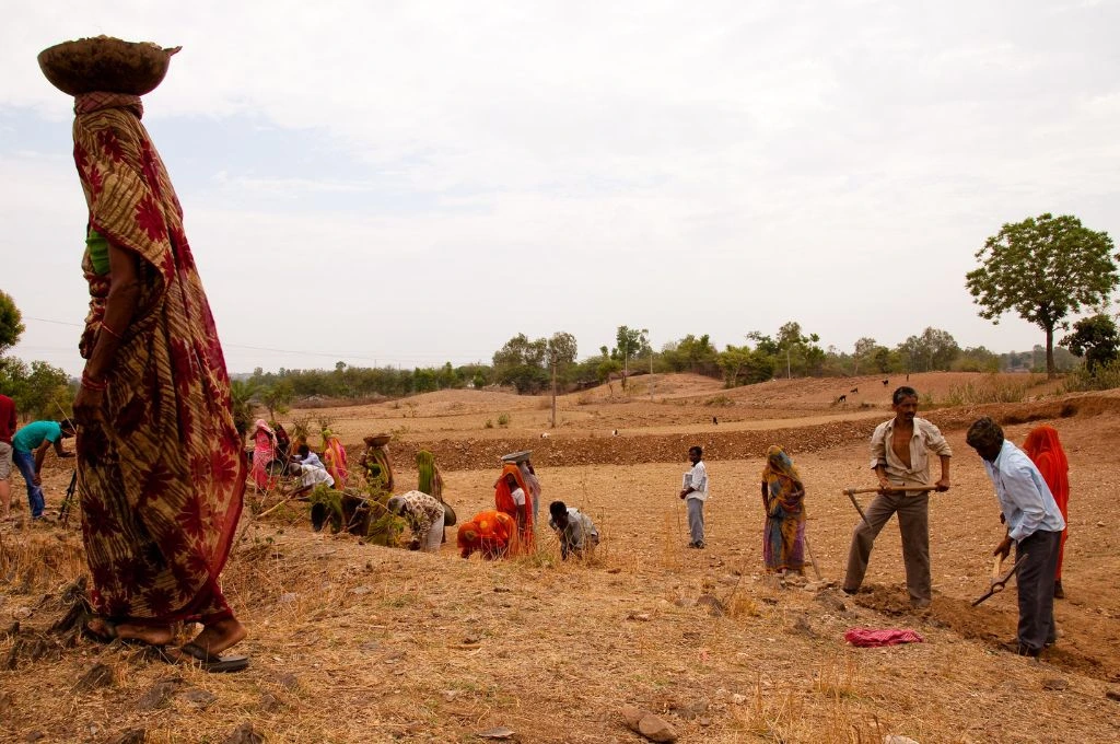 Work in progress at an NREGA site with one female worker carrying a bucket on her head and many other workers in the background--grievance redressal mechanisms