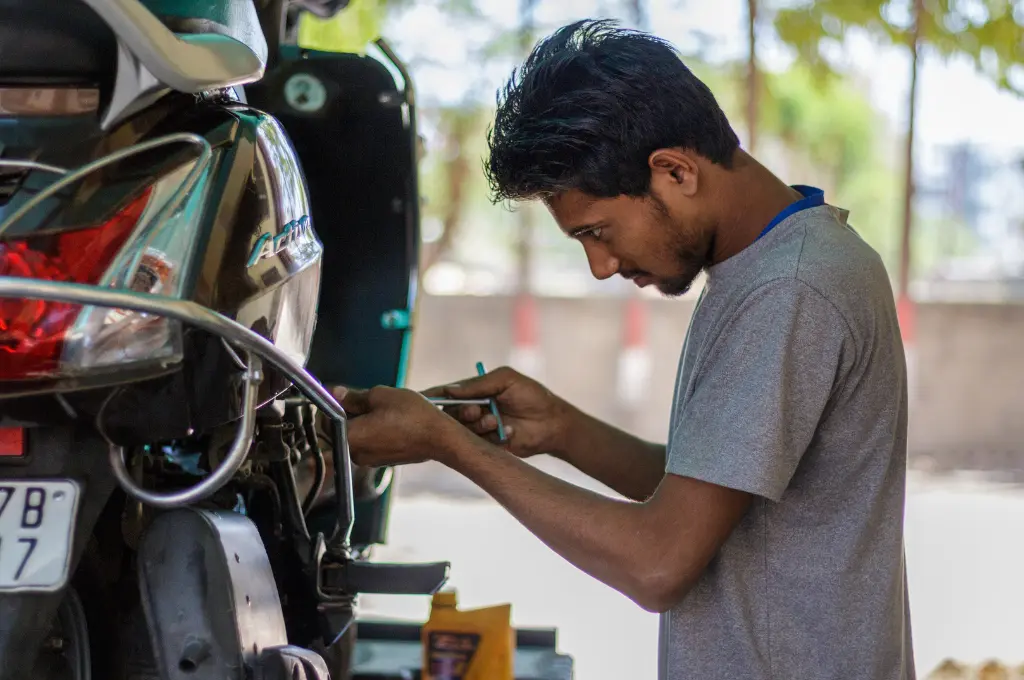 a young man in a grey T-shirt holding a T spanner and repairing a black scooter--skilling for rural entrepreneurs
